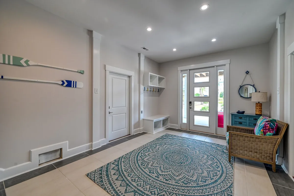This image shows a bright and cheerful entryway with decorative oars, an intricate area rug, a vivid entry door, and a cozy chair. The decor is inviting and sets a friendly and adventurous tone right upon arrival.