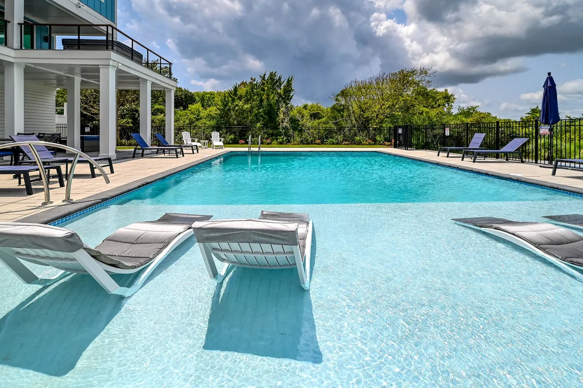 An exterior shot featuring a sparkling swimming pool surrounded by lounge chairs and lush greenery. The spacious deck area is ideal for sunbathing, relaxing, or socializing after a day of island adventures.