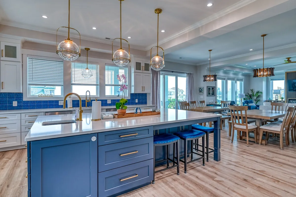 This interior image centers on a spacious kitchen island with stylish blue tile backsplash and hanging lights, opening into the dining area. It visually communicates a chef-inspired kitchen setup designed for cooking, entertaining, and casual family meals.