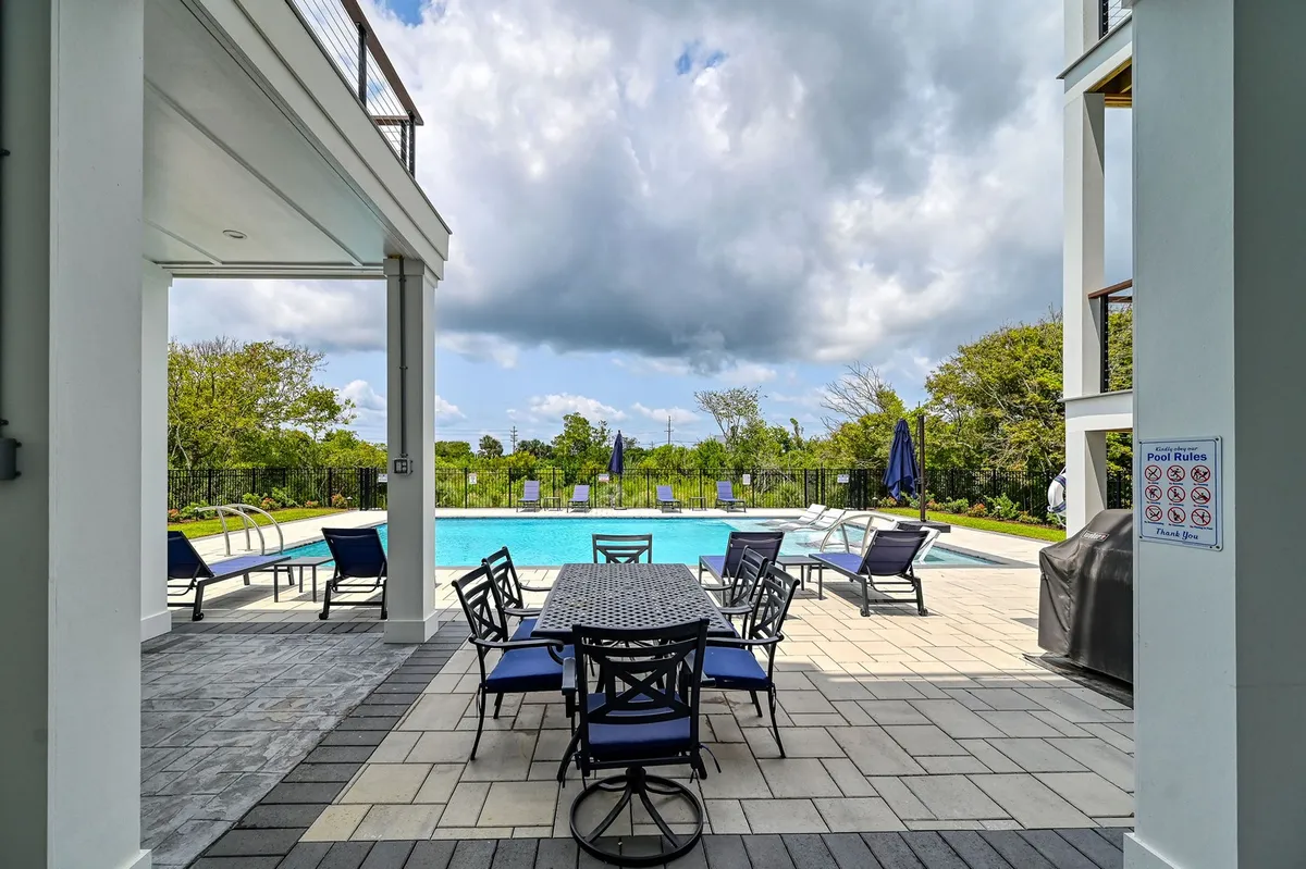 This photo captures the resort-style swimming pool surrounded by comfortable lounge chairs and an outdoor dining area. The poolside deck is expansive, perfect for sunbathing, swimming, and hosting lively social gatherings. The setting suggests both relaxation and celebration, with a relaxed mood and hints of special occasion festivities.