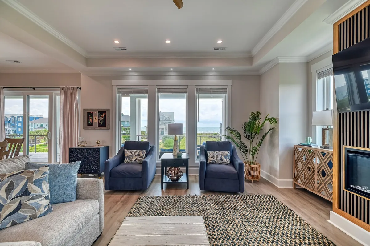 A welcoming living space with two blue armchairs positioned in front of large windows, a wooden coffee table, a decorative plant, and a wall-mounted TV. The scene is awash in natural light, inviting guests to unwind while enjoying views of the outdoors.