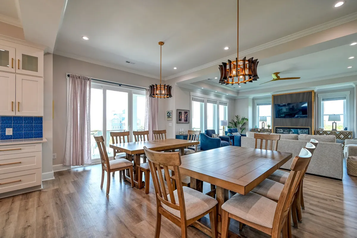 A cozy, well-lit dining space featuring a large dining table, elegant chandelier, comfortable sofa area, and expansive windows. The setting is ideal for shared meals, celebrations, and relaxed group activities, echoing the welcoming, communal spirit of the great room.