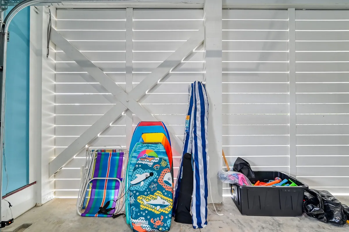 A vibrant and organized equipment room filled with colorful beach gear, a striped umbrella, and stacked chairs. The scene radiates readiness for fun and group activities, emphasizing the beach and sports convenience for guests.