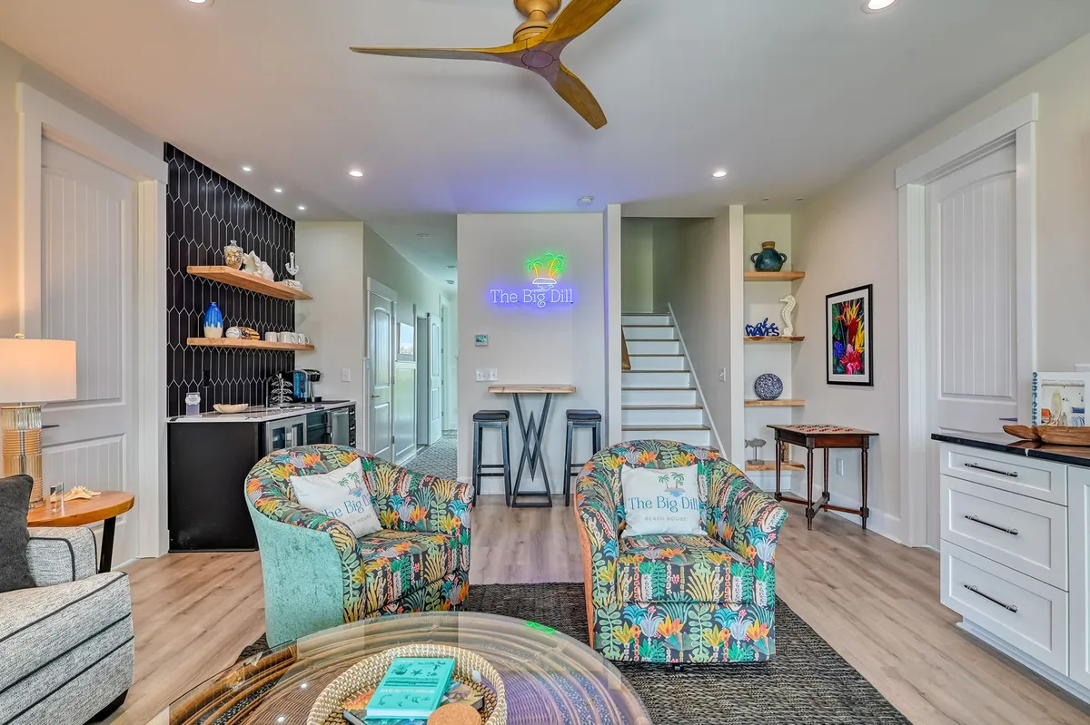 A playful and stylish recreation lounge featuring colorful armchairs, a distinctive neon sign reading 'The Big Dill,' decorative shelving, and a stylish ceiling fan. The arrangement encourages casual conversation and fun evenings, creating a youthful, energetic vibe.