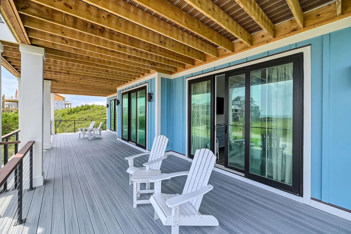 This exterior image highlights a tranquil area with Adirondack chairs facing large glass doors and the blue exterior of the home. The space invites guests to relax, socialize, or enjoy morning sunrises and evening stargazing, enhancing the sense of privacy and luxury.