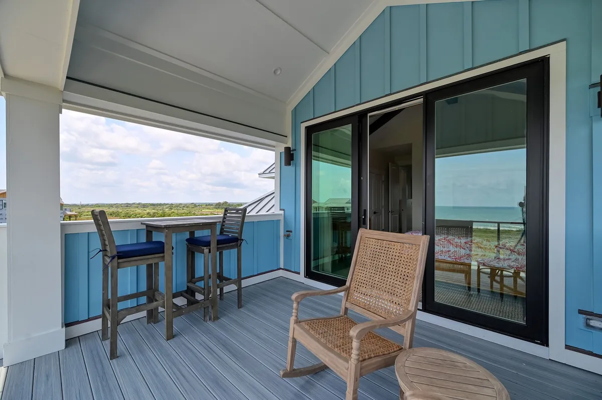 An inviting exterior space featuring a bistro table and woven chair positioned by large glass doors. This area is perfect for enjoying a morning coffee, reading, or gathering with friends while watching sunsets or sipping drinks in the evening breeze. The seamless indoor-outdoor flow sets the stage for relaxed social moments.