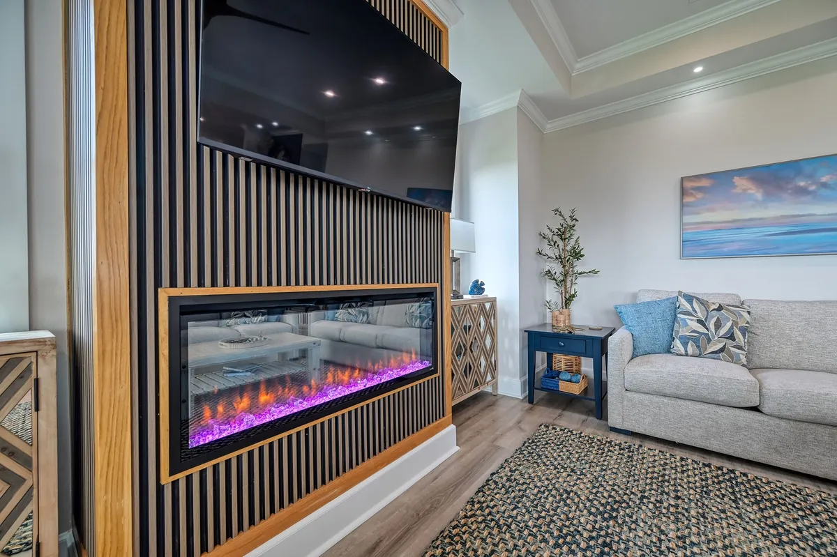 A cozy living area featuring an electric fireplace, television, and comfortable sofa. Framed artwork adorns the walls, and the mood is intimate and inviting, ideally suited for gathering with friends or family to relax, share stories, or enjoy quiet evenings when the weather turns cooler.