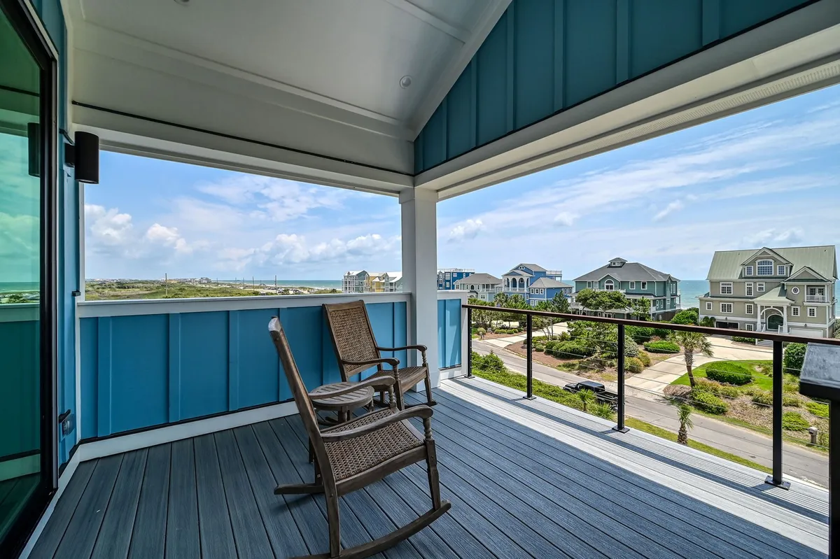An exterior porch scene with classic rocking chairs facing a sweeping ocean view, framed by blue house walls. The porch offers a tranquil space for sipping coffee, reading, or sharing cocktails while enjoying the sea breeze and sunsets.