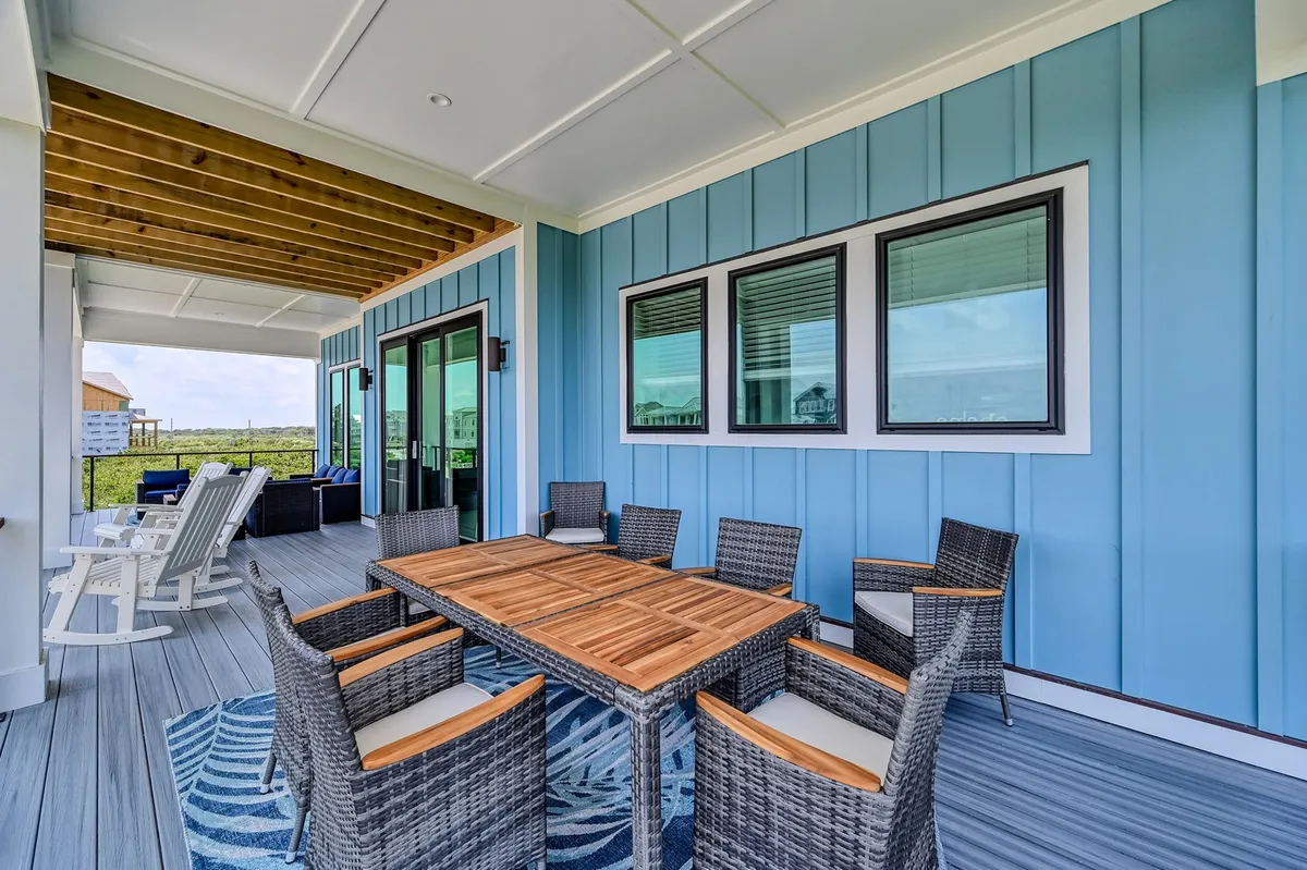 A welcoming outdoor dining area with a table, rattan chairs, blue walls, and a wooden ceiling. The relaxed, open-air setting suggests opportunities for shared meals, sunset dinners, or social gatherings in a space that transitions seamlessly between inside and out.