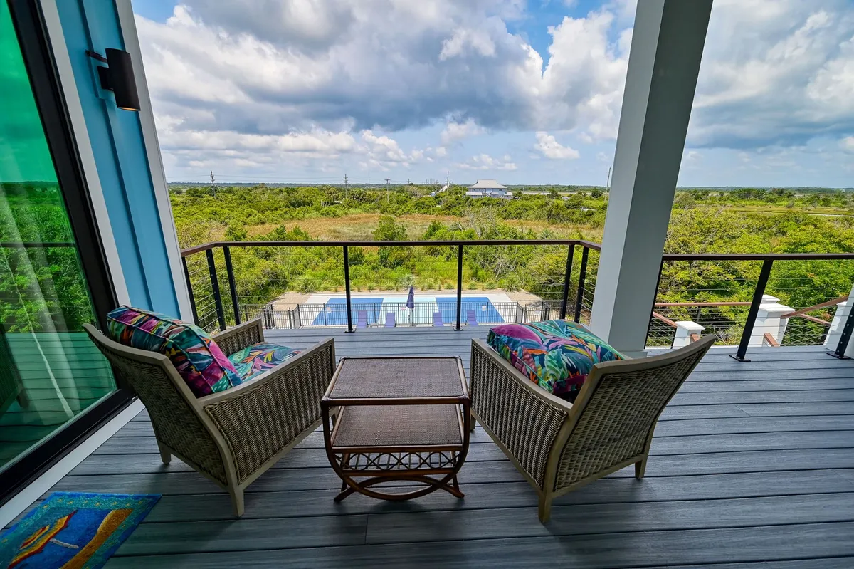 A serene outdoor scene presenting a swimming pool bordered by lush greenery. The outdoor seating area invites relaxation and socializing, while the distant horizon hints at the ocean beyond. The setting is both tranquil and inviting, ideal for sunbathing, sipping coffee, or enjoying sunset views.